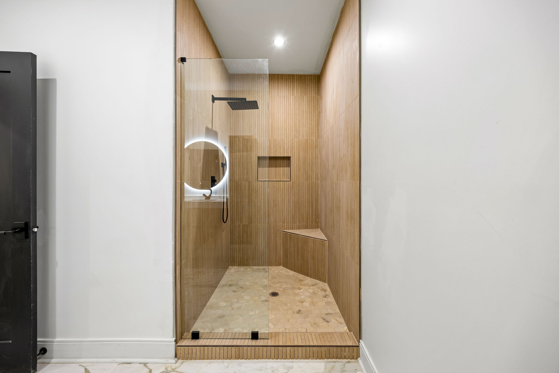 Shower with fluted oak tile, pebble floor and matte black fixtures