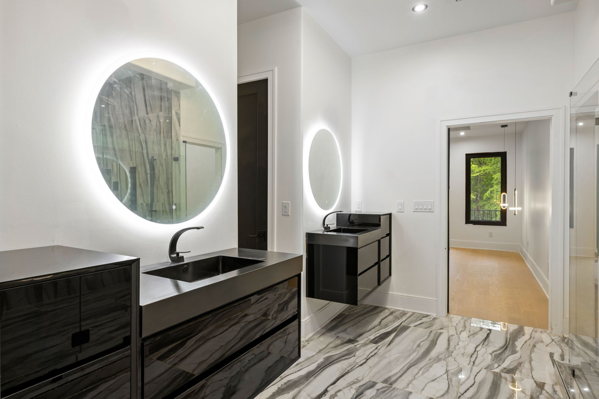 Primary bath with backlit round mirrors and marble tile floors