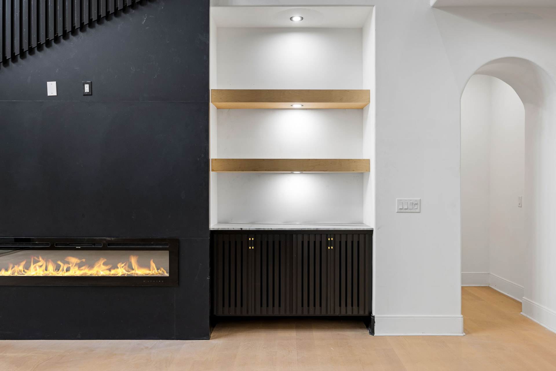 Living room linear fireplace with black stone surround and oak floating shelves