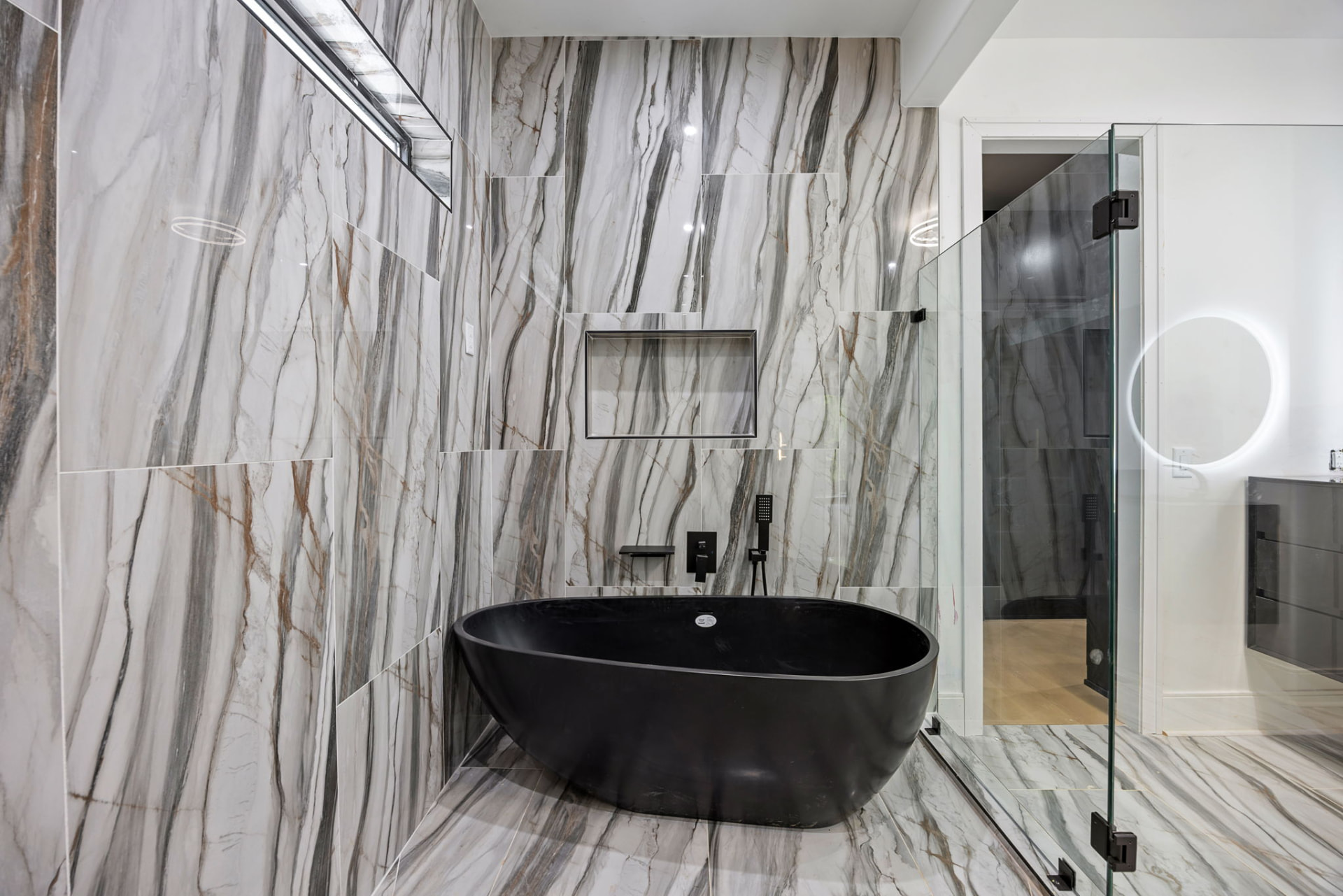 Primary bath with book-matched marble walls and black freestanding tub