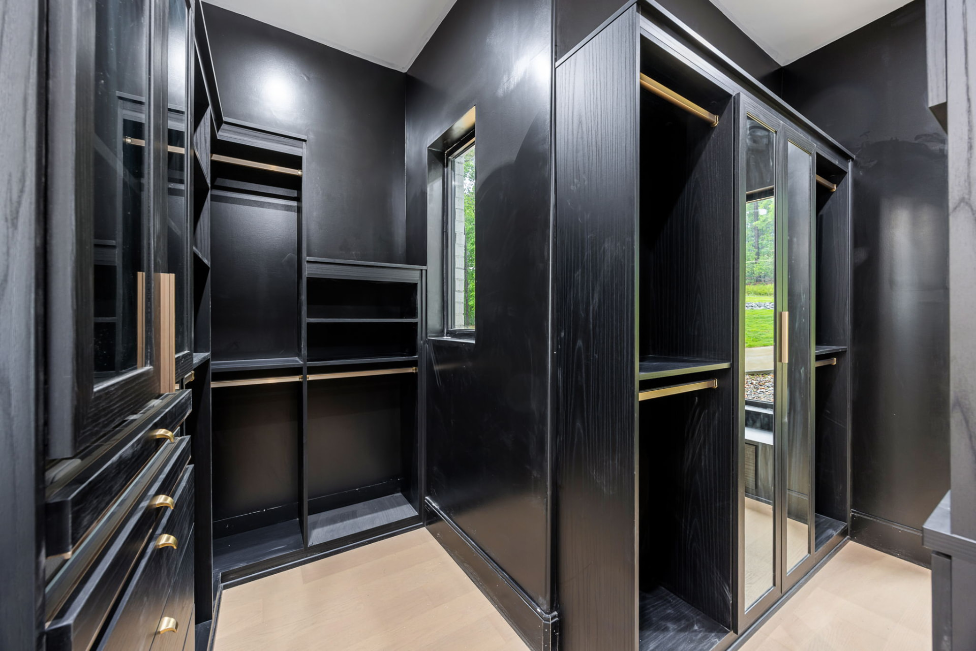 Custom black walk-in closet with brass rods and glass-front cabinets