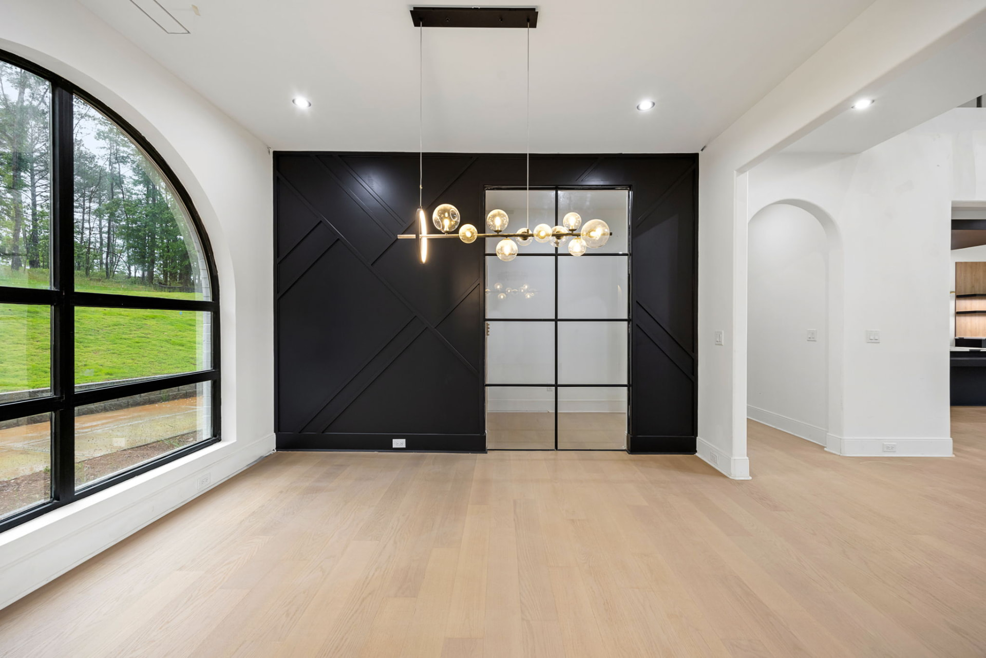 Dining room with black paneled accent wall, arched window and brass globe chandelier