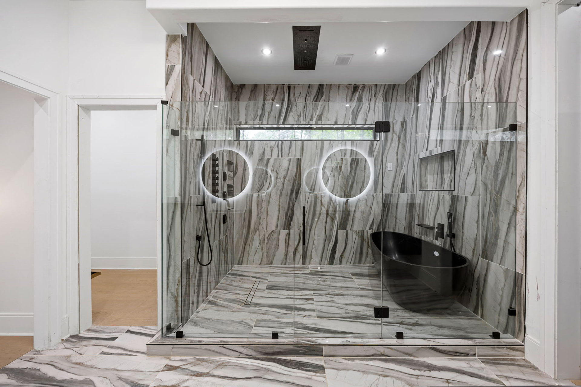Primary bath wet room with book-matched marble, black soaking tub and backlit mirrors