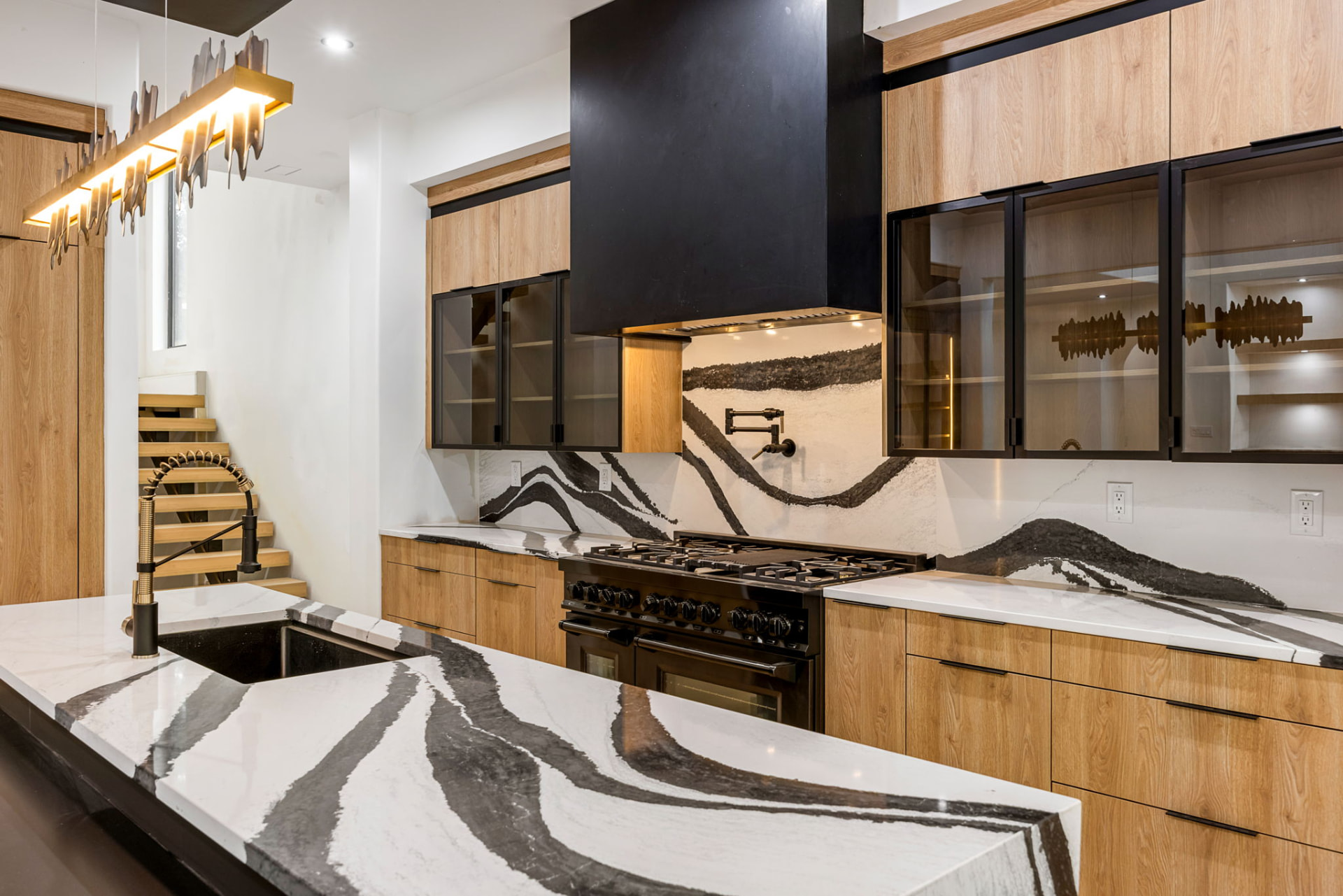 Kitchen with dramatic veined quartz backsplash, black hood and brass pot filler