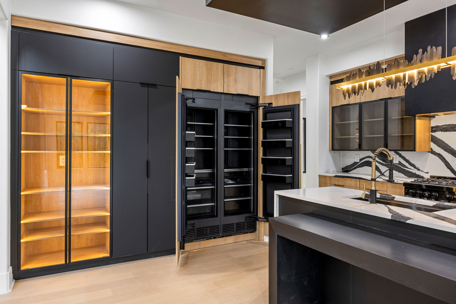 Kitchen with black and white oak cabinetry, lit glass pantry and brass fixtures