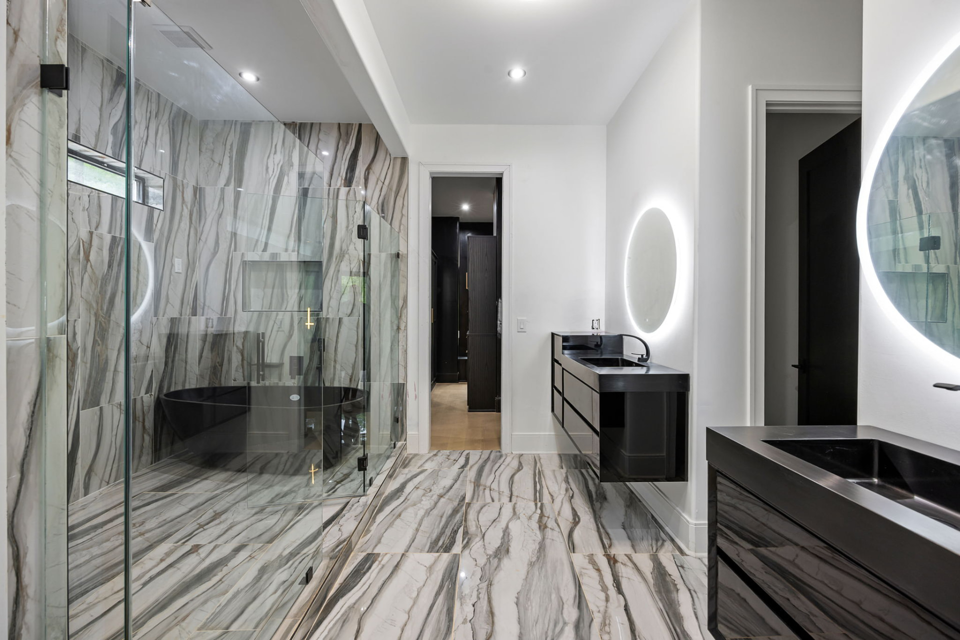 Primary bath with marble slab shower, freestanding black tub and floating vanities