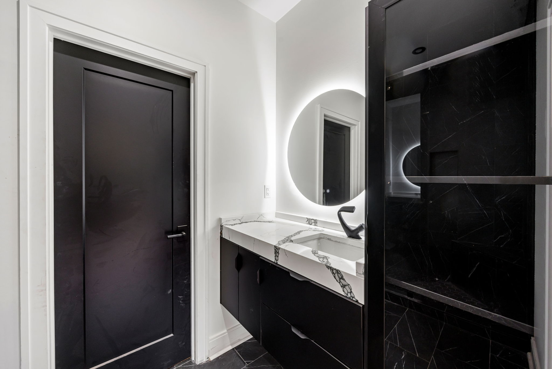 Guest bath with backlit round mirror, black vanity and marble counter